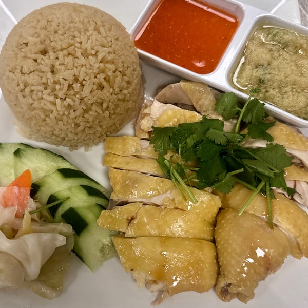 Hainanese chicken rice with sliced chicken, rice, cucumber, pickled vegetables, and two dipping sauces.