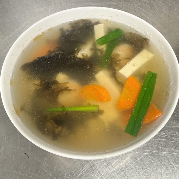 Chinese soup with seaweed, tofu, carrots, and green onions in a white bowl.