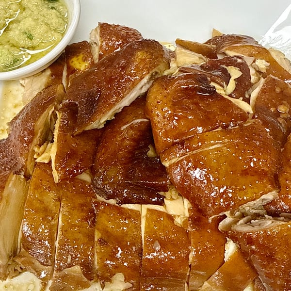 Close-up of chopped Chinese-style roasted chicken with crispy skin, served with a side of green sauce.