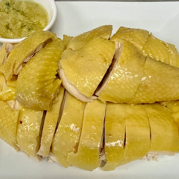 Sliced Hainanese chicken with glistening skin and a side of green ginger scallion sauce.