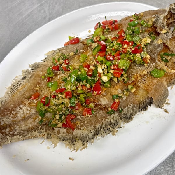 Crispy fried whole fish topped with diced red and green peppers and garlic on a white platter.