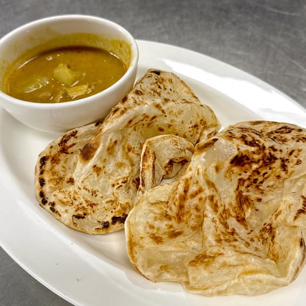 Three pieces of golden-brown roti bread on a white plate, with a side of yellow curry.