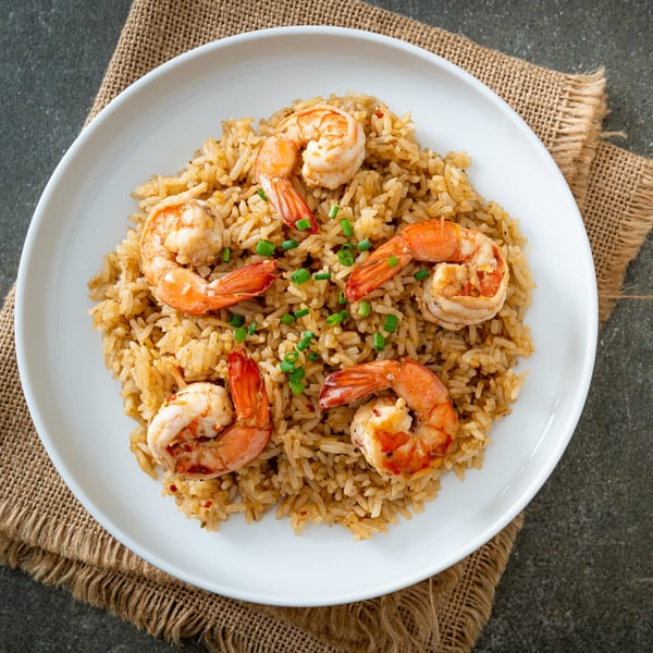 Shrimp fried rice with chopped green onions on a white plate, served on a burlap placemat.